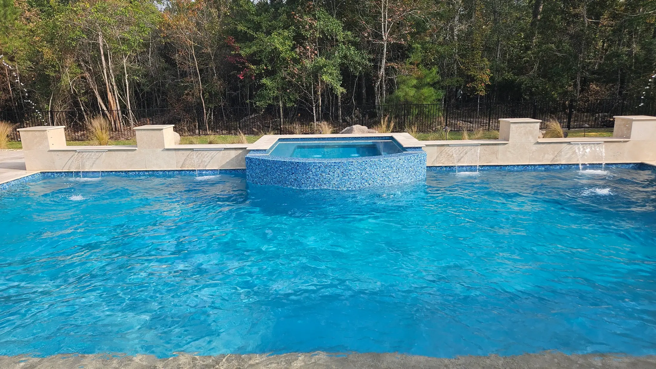 Blue mosaic tile on a Clearwater raised spa above a custom pool with pale stone coping