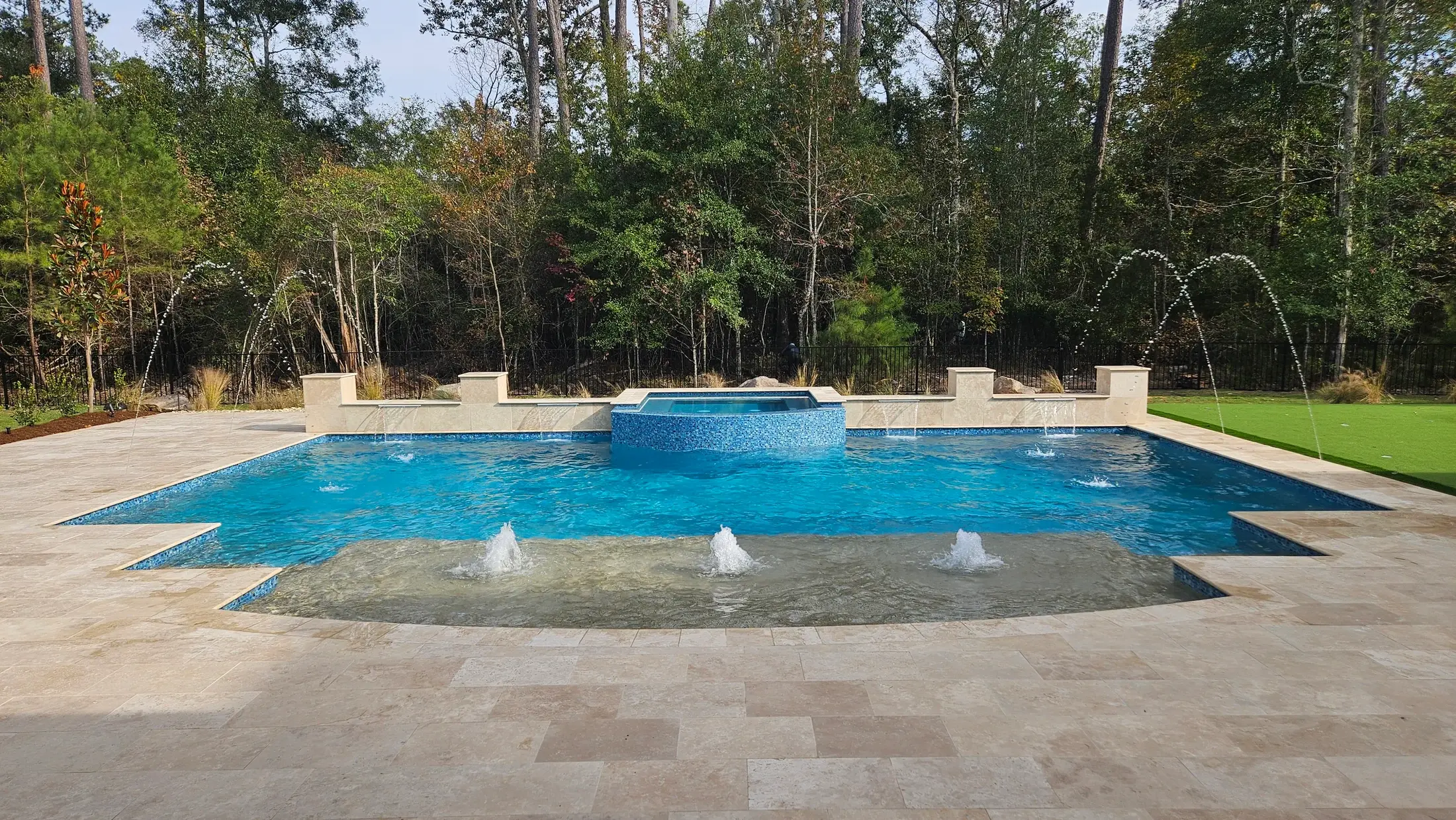 Clearwater custom pool with tanning ledge bubblers, a raised blue mosaic spa, and a stone terrace